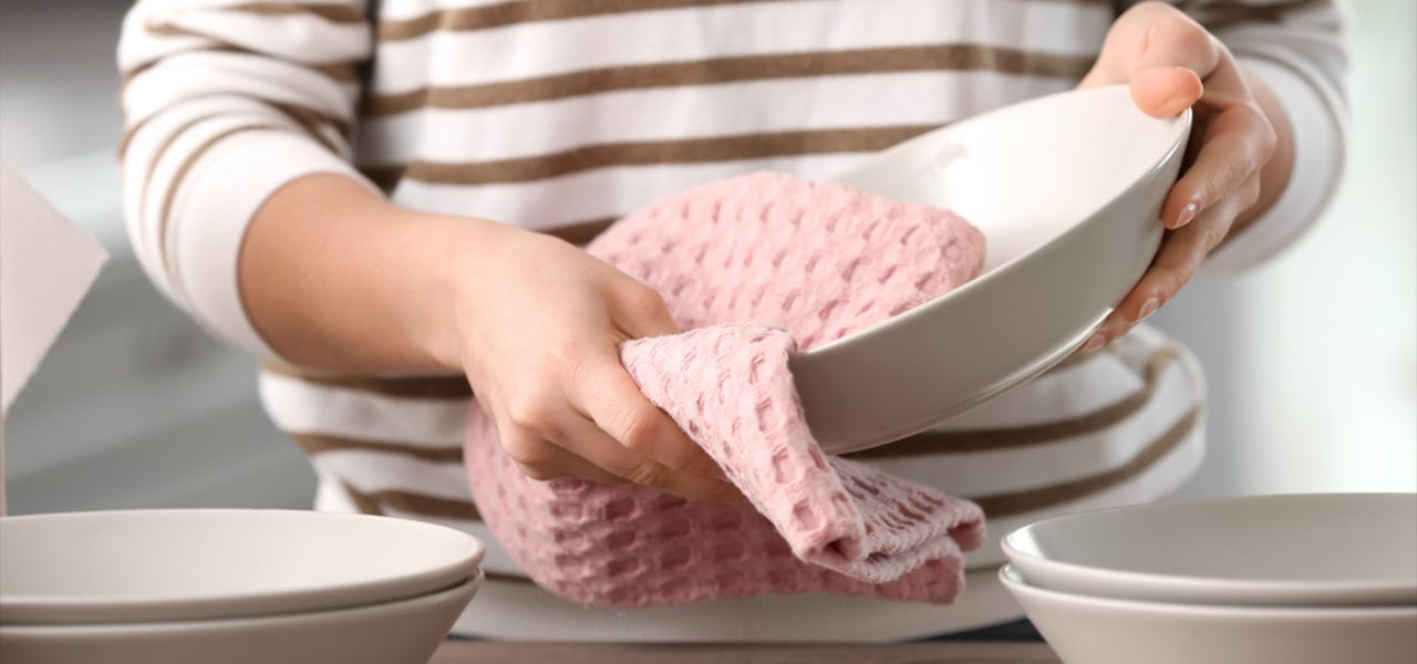hands drying a plate with a pink dish towel