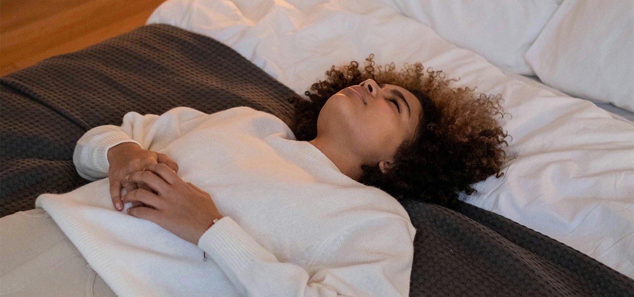 woman resting on her back on a made bed