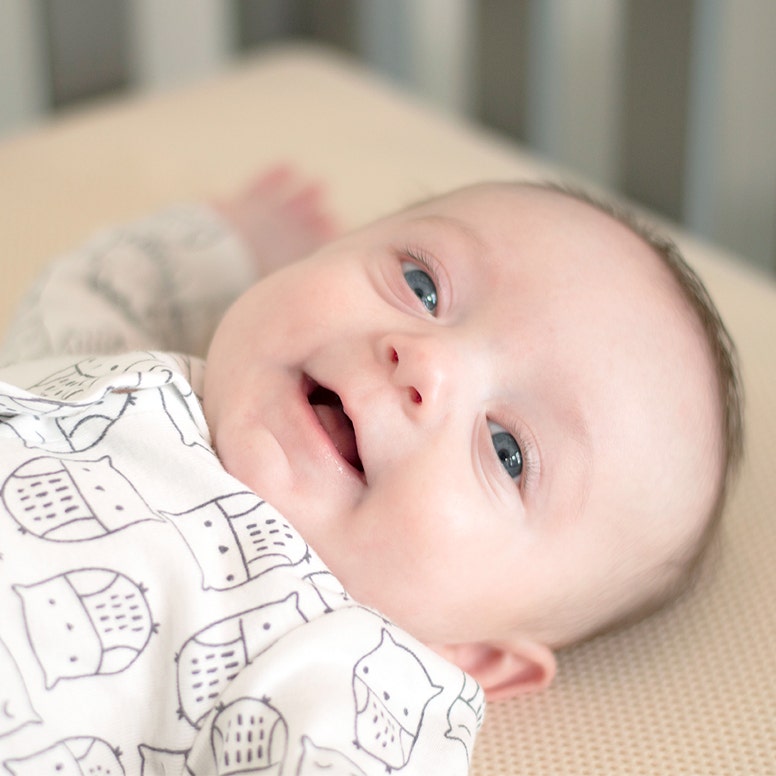 Close-up of baby laying on breathable crib mattress smiling