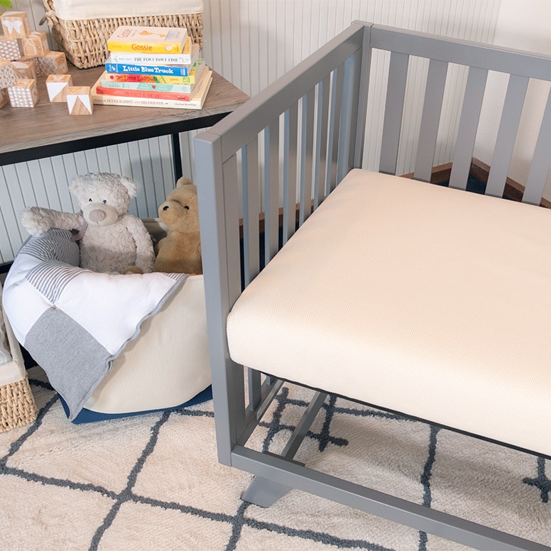 Crib mattress in grey crib in nursery setting