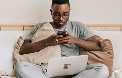 Man sitting up in bed and researching when to replace his mattress